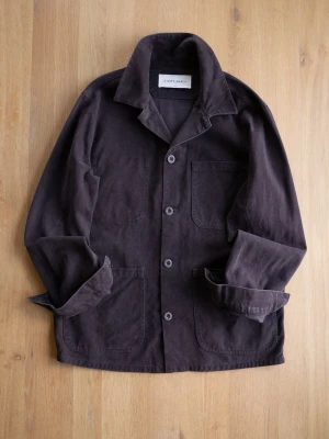 Mörkbrun Chore Jacket från A Day's March - Stilren mörkbrun overshirt från A Day's March i mjuk bomullscanvas. Klassisk krage, tre stora utanpåfickor och knäppning med fyra knappar framtill. Perfekt lager-på-lager-plagg med avslappnad passform och uppvikta ärmar.