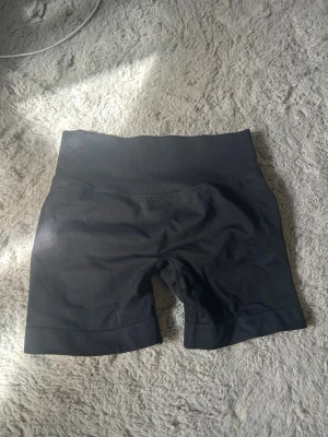 svarta tränings shorts - Säljer ett par svarta tränings shorts med bred ribbad midja och tight passform. Shortsen är tillverkade i ett stretchigt syntetmaterial som passar perfekt till träning eller en sportig look. Storlek S