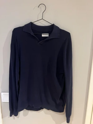 Mörkblå tröja från These Glory Days - Mörkblå långärmad tröja från These Glory Days i storlek medium. Tröjan har klassisk krage och är tillverkad i ett mjukt, ribbat material. Perfekt för en stilren och avslappnad look.
