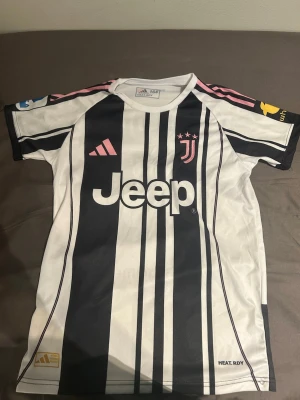 Juventus matchtröja svartvit - Juventus officiella matchtröja från Adidas i svartvitt med rosa detaljer. Tröjan har klassiska ränder, Jeep-logga på bröstet och Yildiz samt nummer 10 på ryggen. Tillverkad i funktionsmaterial HEAT.RDY för bästa komfort under träning eller match.