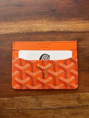Orange korthållare - Snygg orange korthållare med det klassiska mönstret och flera fack för kort. Tillverkad i canvas och läder, perfekt för dig som vill ha en stilren och exklusiv accessoar. Kommer i originalask med dustbag.