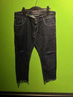 Jacob Cohen jeans - Snygga mörkblå jeans med croppad passform och råa, fransiga benslut. Jeansen har fem fickor, kontrastsömmar och klassisk knappgylf. Perfekta för en avslappnad och trendig look.