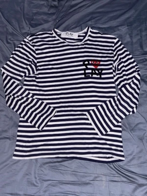 Randig långärmad t-shirt från Comme des Garçons - Säljer en marinblå/vit randig långärmad t-shirt från Comme des Garçons Play med det klassiska hjärta-ögon-trycket på bröstet. Mjuk bomull och relaxed fit, perfekt till jeans och allt möjligt.