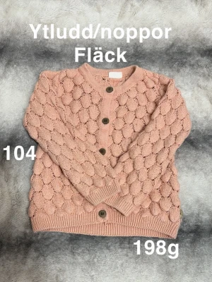 Rosa stickad kofta med bubbelmönster - Supersöt rosa stickad kofta med unikt bubbelmönster och stora träknappar framtill. Koftan har rund halsringning, långa ärmar och ribbade muddar vid ärmslut och nederkant. Perfekt för lager-på-lager och ger en trendig look.🌸 Ytludd/noppor. En fläck. Storlek 104 