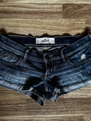 Mörkblå jeansshorts från Hollister - Säljer ett par mörkblå lågmidjade denimshorts från Hollister med slitna detaljer och uppvikta benslut. Klassisk femficksmodell med knapp och dragkedja framtill samt snygga sömmar och logga på bakfickan. Perfekta för alla tillfällen! Säljer då dom tyvärr är för små men dom är super snygga!! Pris kan diskuteras💕💕