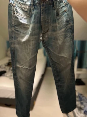 Blå raka jeans med slitningar från acne - Säljer ett par blå jeans med raka ben och lätt slitna detaljer på framsidan. Jeansen har klassisk femficksdesign och är gjorda i denim med en tvättad look. Perfekta för en avslappnad och trendig stil. Nått längd 97cm och midja runt 41