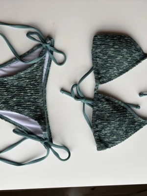 Grön bikini med knyt från Shein storlek S - Snygg grön bikini med ribbad struktur och knyt i sidorna samt i ryggen och nacken. Klassisk trekantsmodell på överdelen och matchande underdel. Perfekt skick! Från Shein storlek S