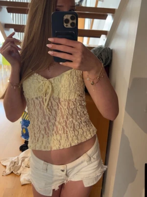 Gul spetsig topp med rosett - Söt ljusgul linnetopp i spets med transparent material och en liten rosett framtill. Toppen är ärmlös och har en figurnära passform som ger en feminin vibe. Perfekt för dig som vill ha en trendig och luftig topp till sommaren. Aldrig använd, prislapp kvar och slutsåld på nätet🤗
