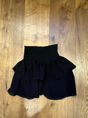 Svarta volangshorts från Chelsea - Säljer ett par svarta shorts från Chelsea i storlek XS. De är med bred smock i midjan och har dubbla volanglager som ger en flowy och trendig look. Perfekta för sommarens alla tillfällen!