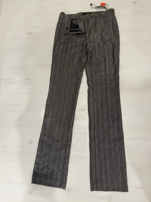 Grå kostymbyxor från Mango Suit - Snygga grå kostymbyxorfrån Mango Suit i storlek 36. Byxorna har ett klassiskt fiskbensmönster, raka ben och sidofickor. Materialet är mjukt och har en elegant struktur som ger en stilren look. Det finns även kavaj som tillhör byxorna men den har storlek 34. Båda är köpa från utlandet.