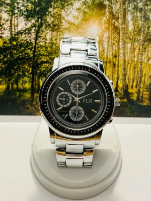 Stilren silverfärgad klocka FLR - Snygg klocka från FLR med svart urtavla och flera dekorativa subdials. Armbandet är i blankt silverfärgat metall och boetten har en klassisk rund form. Perfekt accessoar för dig som gillar en stilren och modern look. Nytt batteri, säljes i befintligt skick enligt bilderna!