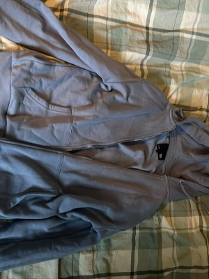 Ljusblå hoodie med dragkedja - Säljer en ljusblå hoodie med dragkedja och fickor framtill. Tröjan har huva med dragsko och ribbade muddar vid ärmslut och nederkant. Perfekt för en avslappnad och chill stil.