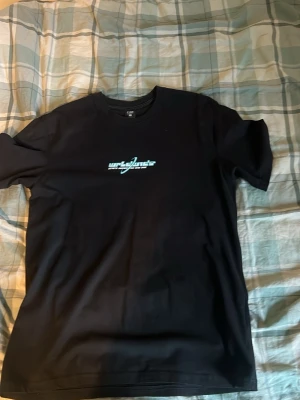 Svart t-shirt med turkost tryck - Säljer en svart t-shirt med turkost och vitt tryck framtill och stort grafiskt tryck på ryggen med texten 'wrld wide' och en planet med ringar. T-shirten har rund hals och korta ärmar. Perfekt för dig som gillar streetwear och coola prints.