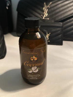 Sunny Isle Coconut olja - Sunny Isle Coconut olja i brun glasflaska med svart skruvlock. Oljan är 100% naturlig och oparfymerad, perfekt för hud och hår. Flaskan har en tropisk etikett med kokosnötmotiv och guldtext.