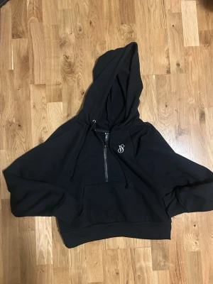 Svart hoodie från Victorias Secret - Svart hoodie med huva, halv dragkedja framtill och en magficka. På bröstet finns VS loggan. Oanvänd. 
