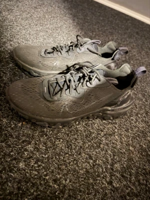 Nike reacts - Säljer ett par svarta Nike Reacts med ventilerande meshmaterial och robust sula. Skorna har snörning, dragflik bak och diskreta detaljer på ovandelen. Perfekta för dig som gillar en sportig och stilren look. Sulorna är även väldigt sköna och skorna är i övrigt i mycket bra skick.
