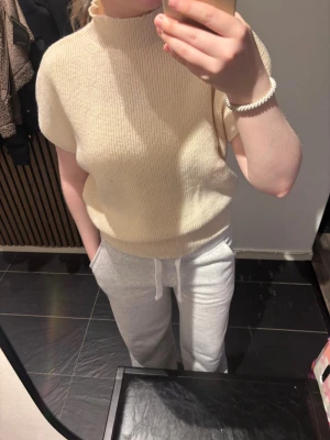 Beige ribbad stickad topp - Krämfärgad stickad topp med ribbad struktur och korta ärmar. Toppen har en hög hals och en relaxed, lite boxig passform. Perfekt för en chill och stilren vibe.