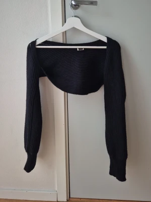 Svart stickad bolero från SHEIN - Säljer en svart stickad bolero från SHEIN i storlek S. Boleron har långa ärmar och är ribbstickad, perfekt att slänga över ett linne eller klänning för extra värme och stil. Materialet är mjukt och stretchigt. Noppig. Hund finns i hemmet. 