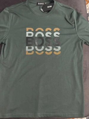 Grön BOSS t-shirt  - Hej, säljer denna boss T-shirt då grön inte passar min dagliga stil samt att den är för stor för mig, den är absolut inte använd utomhus, använt en gång då var det när jag testade den första gången. Inga synliga skavanker och riktigt bra kvalité för en sådan billig t-shirt.
