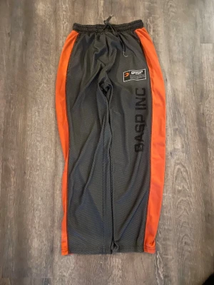 Gasp INC mjukisbyxor svart/orange - Säljer ett par riktigt snygga mjukisbyxor från Gasp INC i svart med orangea sidopaneler. Byxorna har dragsko i midjan, tryckt logga och patch på benet samt sportig meshstruktur. Perfekta för gymmet eller chill hemma. Nästan aldrig använda! 
