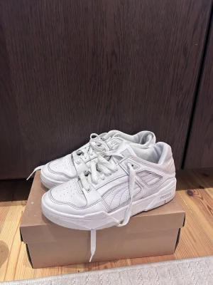 Vita chunky sneakers i läder Puma  - Snygga vita sneakers med chunky sula och klassisk siluett. Tillverkade i läder med perforerade detaljer på tån och sidorna för extra ventilation. Skorna har vita skosnören och en sportig look som passar till många olika stilar.
