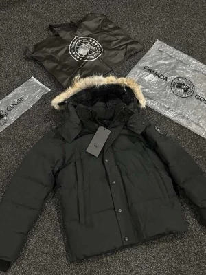 Svart dunjacka med pälskant - Säljer en svart dunjacka från Canada Goose med avtagbar huva och snygg pälskant i beige. Jackan har diskret logga på ärmen, dragkedja och knappar framtill samt flera praktiska fickor. Perfekt för kalla vinterdagar och riktigt varm.