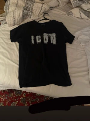Svart ICON t-shirt från Dsquared2 - Storlek L men sitter som M passar båda. Svart t-shirt från Dsquared2 med trycket 'ICON' i vitt framtill. Klassisk passform och rund halsringning. Perfekt för dig som gillar streetwear och vill ha en statement-tee i garderoben.