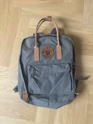 Kånken No. 2 - Fjällräven ryggsäck ”Kånken No. 2” i en grå färg med läder-band. Cirka 4 år gammal och nypris är cirka 1799kr. Använd men i bra skick, endast ett litet hål undertill (se bild). Väskan är även namnad inuti på lappen.