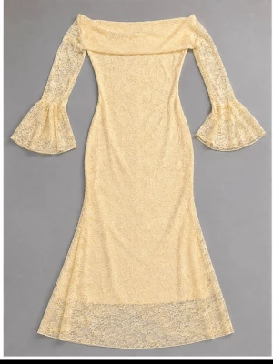 Ljusgul lång spetsklänning offshoulder - Elegant långklänning i ljusgul spets med offshoulder-design och vida trumpetärmar. Klänningen har figurnära passform och vackra spetsdetaljer över hela plagget. Perfekt för dig som vill sticka ut med en romantisk look.