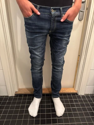 Blå slim fit jeans från Dondup - Säljer ett par blå slim fit jeans från Dondup med snygga slitningar och kontrastsömmar. Jeansen har klassisk femficksmodell och är tillverkade i stretchigt denimtyg för en bekväm passform. Perfekta för dig som gillar en smal siluett och trendig look.