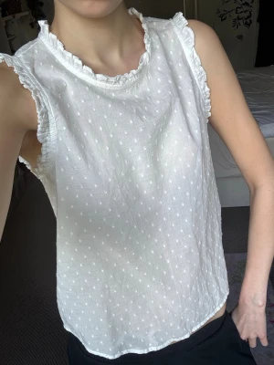 Vit prickig ärmlös blus med volang - Söt vit blus med små prickar och volangdetaljer vid halsringningen och ärmöppningarna😻 Blusen är ärmlös och har en lätt och luftig känsla, perfekt för varma dagar! Tillverkad i mjukt tyg som känns skönt mot huden⭐️Materialet är lite genomskinligt/see thru men det är så designen ska vara🩷Storlek XS från VeroModa, helt oanvänd då jag fick i present med ej gillar.. Väldigt coquette topp som passar fint med jeans och andra plagg! Bra till vardag eller finare events🌺Nypris 249kr!