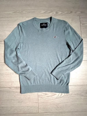 Stickad Hollister tröja - ✅Stickad tröja från Hollister med rund halsringning och broderad logga på bröstet.✅ Tröjan har ribbade muddar vid ärmslut och nederkant, vilket ger en klassisk och stilren look. 💯Perfekt för lager på lager och enkel att matcha.💯Färgen är grå/ljusblå. 📦skickar snabbt o kan gå ner i pris vid snabb affär💨
