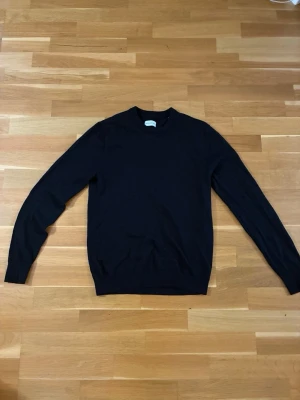 Svart basic tröja - En stilren svart tröja med rund halsringning och långa ärmar. Tröjan har en enkel design utan synliga detaljer och är perfekt för lager-på-lager. Materialet är 100% merinoull, vilket gör den skön att bära.
