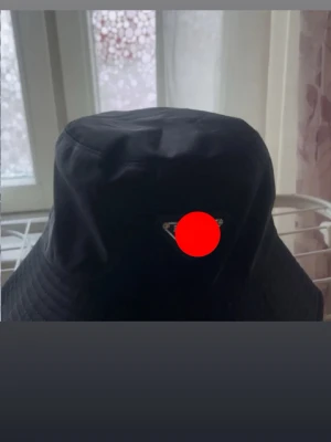 Svart bucket hat med metallogo - Stilren svart bucket hat med en liten metallogo framtill. Hatten har klassisk form med mjuk brätte och är tillverkad i ett slätt tyg som ger en modern look. Perfekt accessoar för att lyfta din outfit.