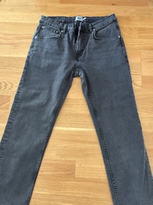 Grå raka jeans med fem fickor - Säljer ett par grå jeans med rak passform och klassisk femficksdesign. Jeansen har bälteshällor, knappgylf och är tillverkade i ett mjukt denimtyg. Perfekta för en avslappnad och stilren look.