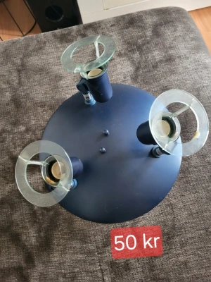 Modern taklampa med tre spotlights - Säljer en rund taklampa i mörkblå metall med tre justerbara spotlights. Lampan har detaljer i glas runt varje ljuskälla och kopplingskablar på baksidan för enkel installation. Passar perfekt för dig som vill ha en stilren och modern belysning. Plasten har smält lite som man kan se på bilderna.