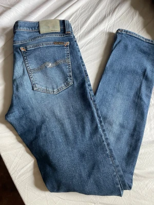  Nudie Jeans - Säljer ett par klassiska blå jeans från Nudie Jeans med snygg tvätt och diskret slitning. Modellen har raka ben och fem fickor, samt Nudie Jeans signaturbroderi på bakfickan. Perfekta till vardagslooken! Jag är 185 lång passar mig perfekt 