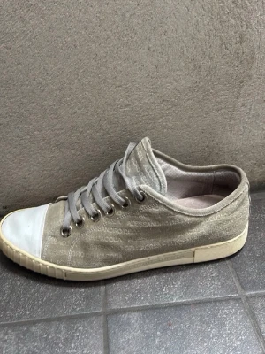 Grå låga sneakers Ifrån Italien - Säljer ett par grå sneakers ifrån Italien med lågt skaft och vita tåhättor. Skorna har textmönster över hela ovandelen och grå snören. Yttermaterialet ser ut att vara tyg och sulan är i gummi. Perfekta för en avslappnad och stilren look.