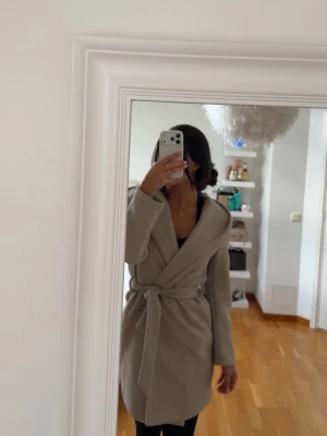 Beige omlottkappa med knytskärp - Snygg beige kappa i omlottmodell med brett knytskärp i midjan. Kappan har en klassisk krage och går ner till mitten av låret. Perfekt för dig som vill ha en stilren och enkel look till hösten eller våren. ZARA