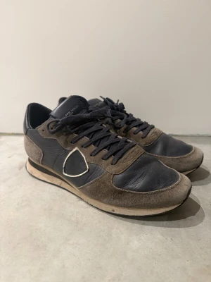 Philippe Model sneakers i mocka och skinn - Snygga sneakers från Philippe Model i mörkblått skinn och brunt mocka. Klassisk design med snörning, rund tå och kontrastdetalj på sidan. Perfekta för dig som gillar en stilren men ändå sportig look. St 43