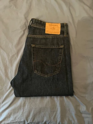 Mörkblå jeans från Jack & Jones - Snygga mörkblå jeans från Jack & Jones med klassisk femficksdesign och raka ben. Jeansen har kontrastsömmar och en läderpatch med logga bak i midjan. Perfekta för en avslappnad och stilren look.