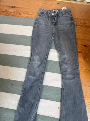 Grå bootcut jeans från ONLY - Snygga grå bootcut jeans från ONLY i modellen Blue Denim. Jeansen har klassisk femficksdesign, normal midja och lätt utsvängda ben. Perfekta till en avslappnad och trendig look. Materialet är mjukt och stretchigt för extra komfort.
