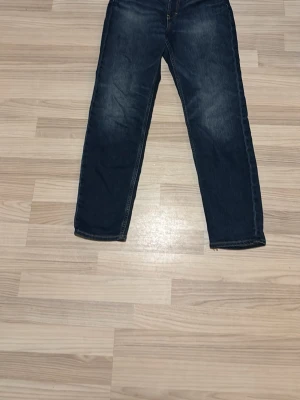 Mörkblå raka jeans - Säljer ett par mörkblå jeans med raka ben och klassisk femficksmodell. Jeansen har subtila slitningar framtill och är tillverkade i ett denimtyg som ger en tidlös look. Perfekta för dig som gillar enkel och stilren stil.