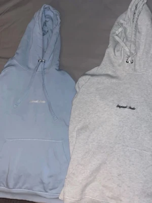 Två hoodies Originals Studio - Säljer två hoodies från Originals Studio, en i ljusblått och en i ljusgrått. Båda har huva med dragsko, magficka och broderad logga på bröstet. Perfekta för chill dagar och streetwear-stil. Säljer båda för 400