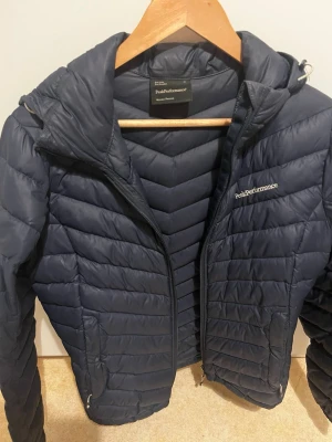  Peak Performance jacka - Snygg mörkblå dunjacka från Peak Performance i dammodell. Jackan har huva, dragkedja framtill och två sidofickor med dragkedja. Quiltad design med horisontella sömmar och diskret logga på bröstet. Perfekt som allvädersjacka. Har några mindre skavanker men de syns inte så jätte mycket därav priset. sparsamt använd och skulle även säga att den passar även S.❤️