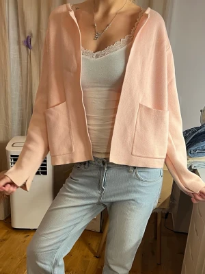 Ljusrosa kofta med fickor - Söt ljusrosa kofta i mjukt stickat material. Koftan har två stora fickor framtill, raka ärmar och en avslappnad passform. Perfekt att slänga över ett linne eller t-shirt för en chill look.