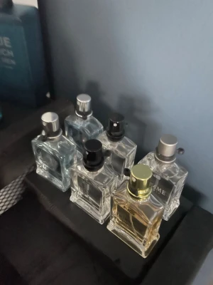 Sex stilrena parfymflaskor i glas - Säljer ett set med sex snygga parfymflaskor i transparent glas. Flaskorna har olika färger på locken, bland annat silver, svart och guld. De har en modern, fyrkantig form och passar perfekt för dig som gillar att variera doft. Perfekt till din parfymhylla!