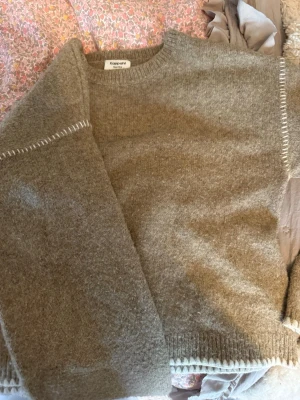 Beige stickad tröja från Kappahl - Mysig beige stickad tröja från Kappahl med rund halsringning och ribbade muddar. Tröjan har diskreta vita detaljer vid ärmslut och nederkant. Perfekt för dig som gillar en enkel och stilren look.