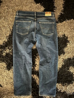 Blå raka jeans från Wrangler - Säljer ett par klassiska blå jeans från Wrangler med rak passform. Jeansen har fem fickor, normal midja och snygga kontrastsömmar. Perfekta för en avslappnad och stilren look. Materialet är slitstark denim i bomull.