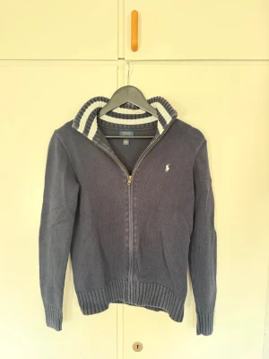 Mörkblå ziptröja från Polo Ralph Lauren - Säljer denna riktigt snygga mörkblåa stickad ziptröja från Ralph Lauren. Den är lite urtvättad i färgen men inga defekter. Storleken är barn L men sitter om XS. Priset ej hugget i sten!